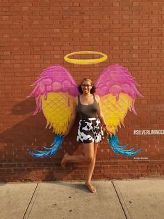 a woman standing in front of a brick wall with an angel wings painted on it