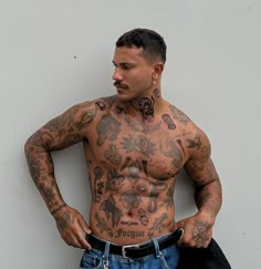 a man with tattoos on his chest standing next to a wall and looking at the camera