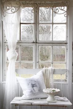 a white bench sitting in front of a window next to a vase with flowers on it