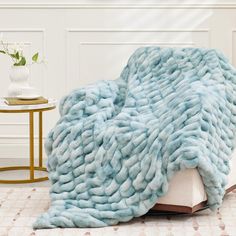 a large blue blanket sitting on top of a white couch next to a table with a vase