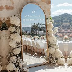 a large mirror sitting on top of a table covered in white flowers and greenery