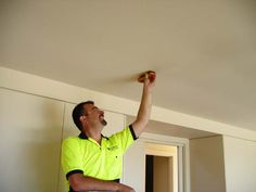 a man in yellow shirt and black pants holding an apple up to the ceiling above his head