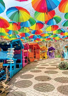 many colorful umbrellas are hanging from the ceiling in an open area with bricks and cobblestones