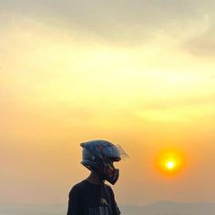 a person wearing a helmet and standing on top of a hill with the sun in the background