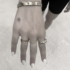 a woman's hand with two rings on it and a small tattoo on the middle finger