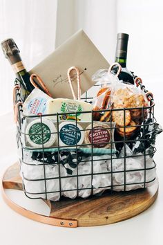 a basket filled with cheese and wine sitting on top of a wooden board