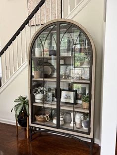 an arched glass cabinet in the corner of a room with stairs and potted plants