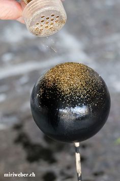 a person is sprinkling gold glitter on a black ball with a wooden skewer