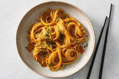 a white bowl filled with pasta and chopsticks on top of a countertop