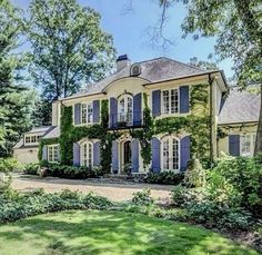 a large house with blue shutters and ivy growing on it's walls, surrounded by trees