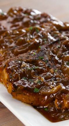 a piece of meat covered in gravy on top of a white square plate