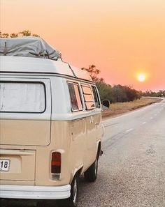 an old vw bus is parked on the side of the road as the sun sets