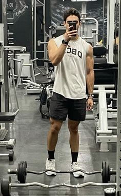 a man is taking a selfie in the gym with his cell phone while standing next to a barbell rack