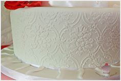 a white wedding cake with red flowers on the top and bottom tier is decorated with icing