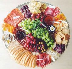 a platter filled with cheese, crackers, grapes and other foods on a table