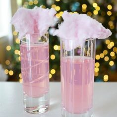 two glasses filled with pink liquid sitting on top of a table next to a christmas tree