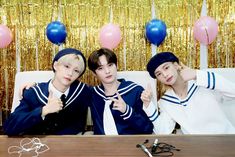 three young men sitting at a table with balloons and streamers in front of them