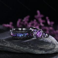 two rings sitting on top of a rock next to purple and blue flowers in the background