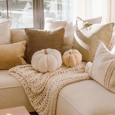 pillows and pumpkins are sitting on a couch in front of a window with a blanket