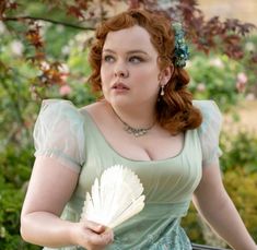 a woman in a green dress holding a white fan and looking off to the side