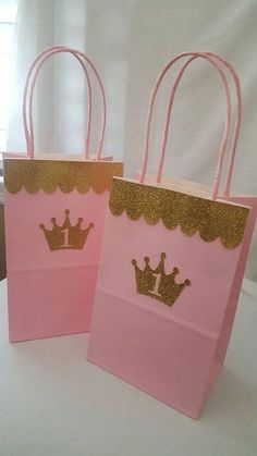 two pink bags with gold crowns on them sitting on top of a white tablecloth