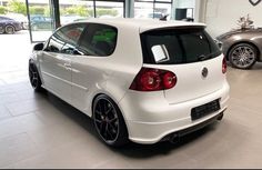 the back end of a white car in a showroom with other cars behind it