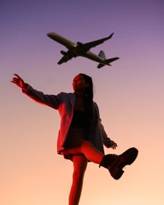 a woman is standing in front of an airplane and looking up at the sky with her arms outstretched