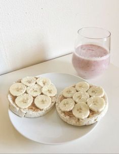 two sandwiches with banana slices and peanut butter are on a plate next to a glass of pink smoothie