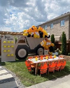 a tractor birthday party with orange and yellow balloons on the back yard, table set up for an outdoor event