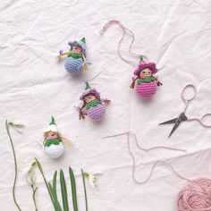 crocheted dolls and yarn are arranged on a table with scissors, thread, and flowers