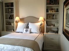 a neatly made bed with two lamps on either side of the headboard and bookshelves