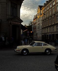 an old car is parked on the street in front of some buildings and people walking around