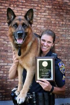 a police officer holding a dog in his lap and posing for the camera with an award plaque