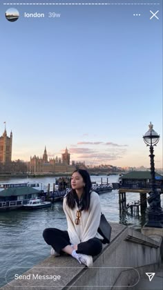 a woman sitting on the edge of a bridge looking up at the sky and buildings