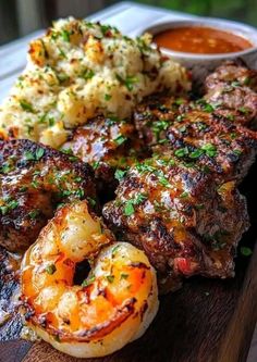 steak, shrimp and mashed potatoes on a wooden cutting board with dipping sauces