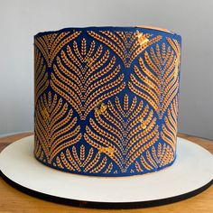 a blue and gold decorated cake sitting on top of a wooden table next to a white plate