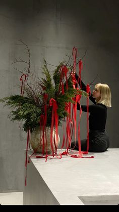 a woman sitting on top of a white table next to a vase filled with plants