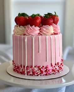 a pink cake with white icing and strawberries on top is sitting on a plate