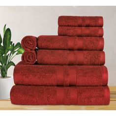 a stack of red towels sitting on top of a wooden table next to a potted plant