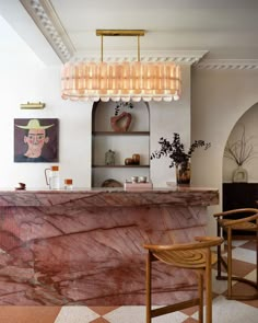 a marble counter top sitting under a chandelier in a living room next to two wooden chairs