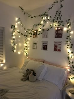 a bed with white sheets and lights on the headboard, along with a teddy bear