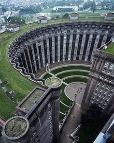 an aerial view of a circular building in the middle of a city with grass on top