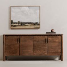 a painting hangs on the wall next to a wooden sideboard with drawers and doors