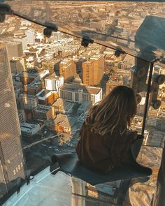 a woman sitting on top of a tall building looking down at the city from above