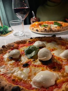 two pizzas sitting on top of a table next to glasses of water and wine