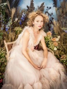 a woman in a dress sitting on a bench surrounded by flowers