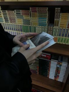 a person is reading a book in front of a bookshelf full of books