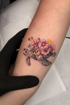 a woman's arm with a turtle and flowers on it