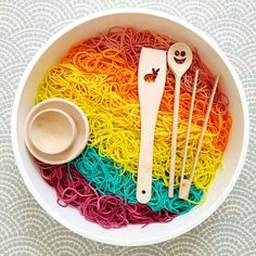 a bowl filled with lots of rainbow colored noodles and wooden spoons next to each other