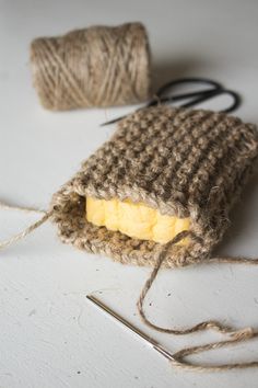 a piece of cloth with yarn and scissors on the floor next to it, which is being used as a knitting tool